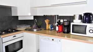 A modern kitchen with white cabinets, a dishwasher, a stove, a sink, and a coffee maker.