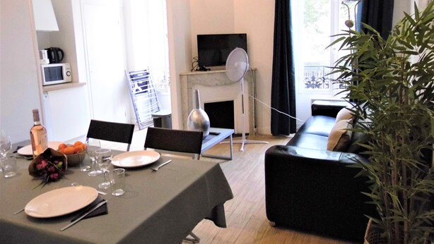 A dining area with a table set for two, a fireplace, a television, and a potted plant.