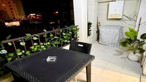 A balcony with a table and chairs, a potted plant, and a covered object. - Cozy 1BR Retreat, Steps to Sand (Sousse)