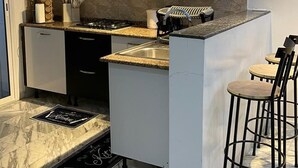 A modern kitchen with white cabinets, a granite countertop, a gas stove, and a small bar area with stools. - Cozy 1BR Retreat, Steps to Sand (Sousse)