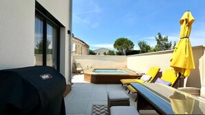Terraza en la azotea con jacuzzi, sillas reclinables amarillas y zona de parrilla cubierta.