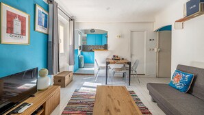 Een moderne woonkamer met een televisie, een houten salontafel en een bank met een decoratief kussen. Op de achtergrond is een eethoek met een tafel en stoelen zichtbaar.