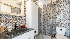 Een badkamer met patroontegels, een wit wastafelmeubel en een douchecabine met glazen wanden.