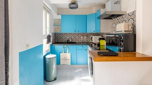 Een kleine keuken met blauwe kastjes, een decoratieve spatwand, een broodrooster en een prullenbak.
