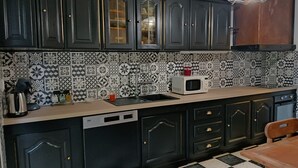 Una cucina con mobili scuri, uno schienale decorato, un forno a microonde e un pavimento a scacchi.