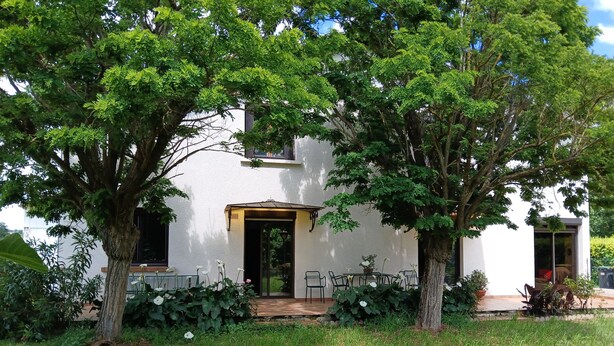 Un edificio bianco con un portico coperto, circondato da vegetazione rigogliosa e alberi.