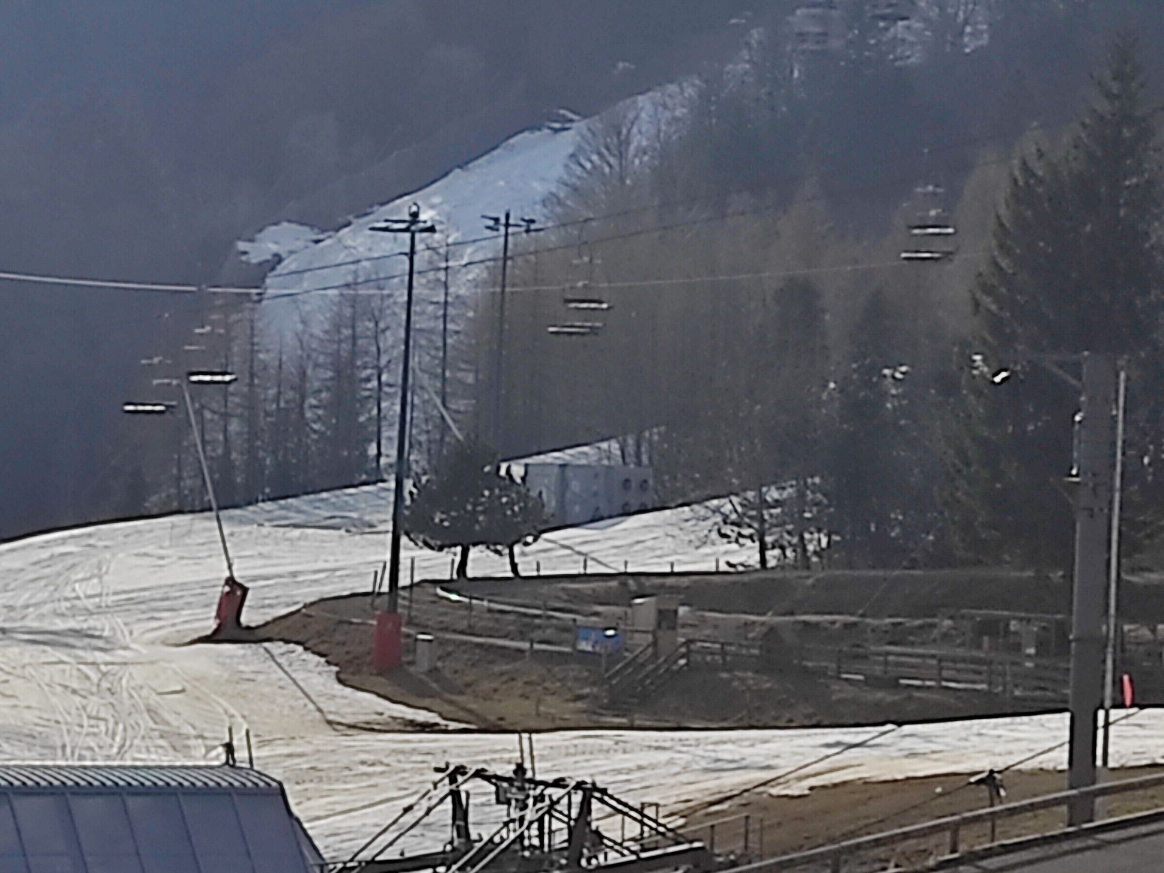 A ski lift with cables and chairs, a snowy mountain in the background, and a clear sky.
