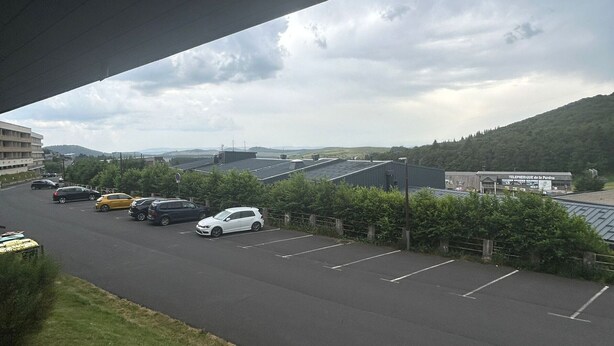 Ein Parkplatz mit mehreren Autos, ein Gebäude mit der Beschriftung "TELEPHERIE de la Perdrie" und eine bergige Landschaft im Hintergrund.