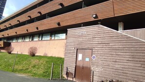 Ein mehrgeschossiges Gebäude mit Holzfassade, einem sichtbaren Eingang und einer Tür, sowie einer Beschilderung darüber.