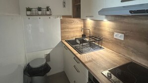 Eine kleine Küche mit weißen Schränken, einer Holz-Spritzschutzwand, einem Spülbecken mit Geschirrgestell und einem Herd.