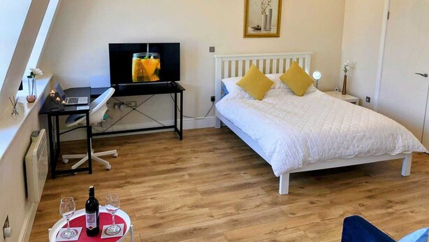 Una camera da letto con un letto, una scrivania con un portatile, una televisione e un tavolo da pranzo con bicchieri da vino e una bottiglia.