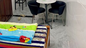 A small room with a bed, a TV mounted on the wall, two chairs, a table, and a door.