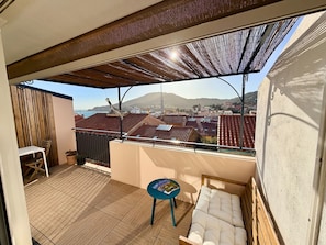 Ein Balkon mit Blick auf eine Stadt, eine Sitzecke mit Sofa, Tisch und Stuhl.