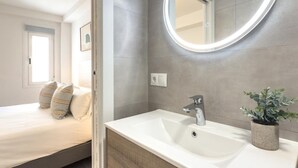 A modern bathroom with a white sink, a round mirror, and a potted plant.