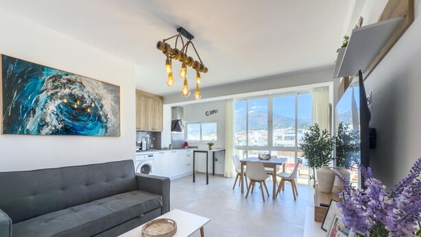 A modern living room with a grey sofa, a white coffee table, and a kitchen in the background.