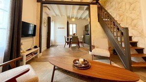 A spacious living area with a wooden coffee table, a TV, and a staircase leading to another level. - Charming cottage in Langeais with terrace and wifi for 4 people (Langeais)