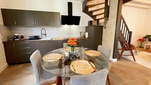 A modern kitchen with dark cabinets, a central island, and a dining area with a glass table and grey upholstered chairs. - Charming cottage in Langeais with terrace and wifi for 4 people (Langeais)