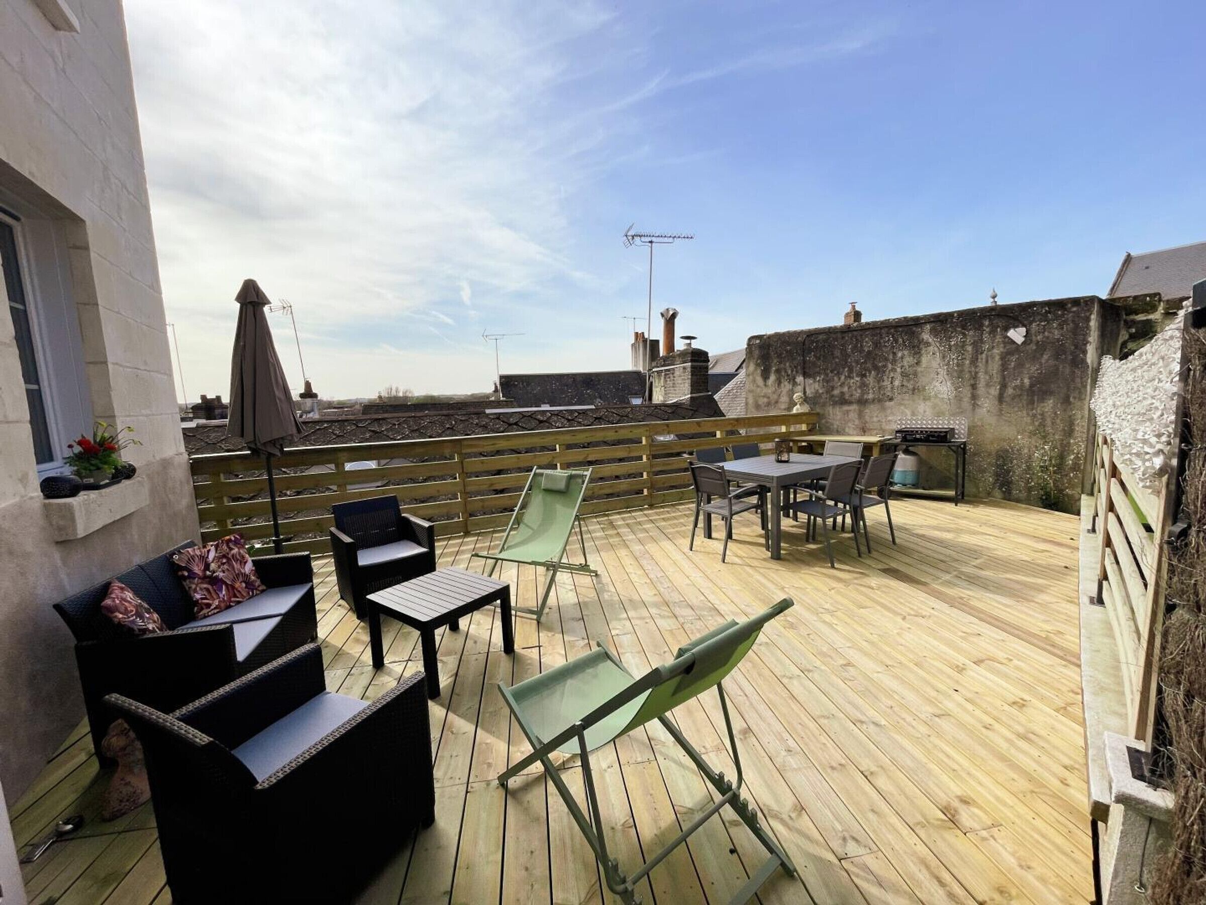 A wooden deck with outdoor furniture, including a table and chairs, and a green lounge chair.