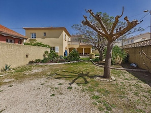 A residential area with a house featuring a tiled roof, a balcony, and a garden with a tree and plants.