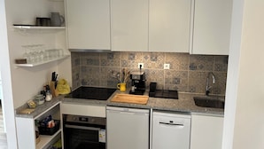 A compact kitchen with white cabinets, a granite countertop, a coffee machine, a sink, and a dishwasher. - Casa da Praceta (Porto)