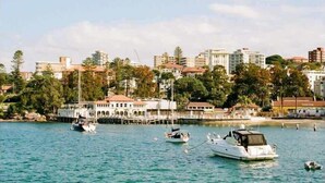 A marina with several boats docked, a white building with a covered area, and a cityscape with buildings and trees in the background.
