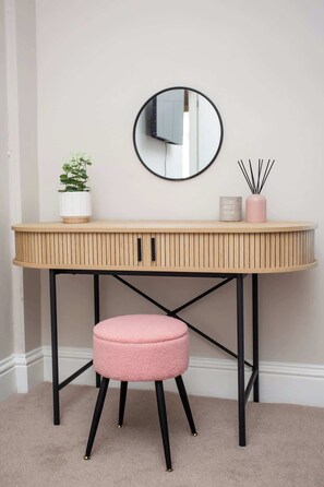 A round mirror, a small potted plant, a pink candle holder, and a stool on a wooden desk with a black metal frame.