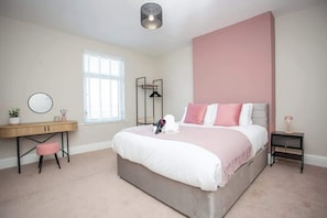 A bedroom with a bed, bedside table, nightstand, desk, chair, and a window.