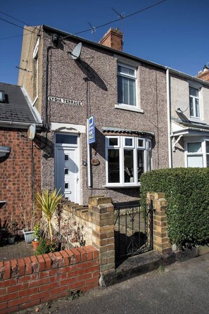 A two-story house with a 'For Sale' sign, a satellite dish, and a gated entrance.
