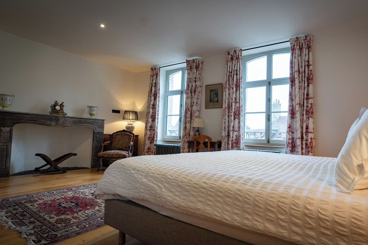 A bedroom with a large bed, a fireplace, a window with curtains, and a rug.