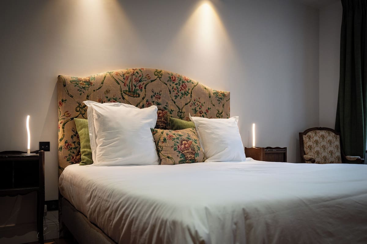A neatly made bed with a floral headboard, two bedside tables, and a chair.