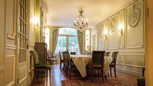 Una sala da pranzo formale con un lungo tavolo, sedie, un lampadario e un tappeto decorato.