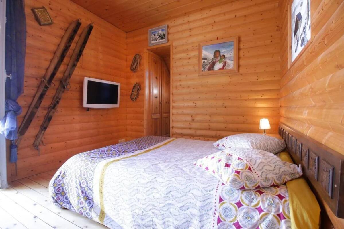 En stuga med träpanel, inredd med en säng, en tv och en dörr.