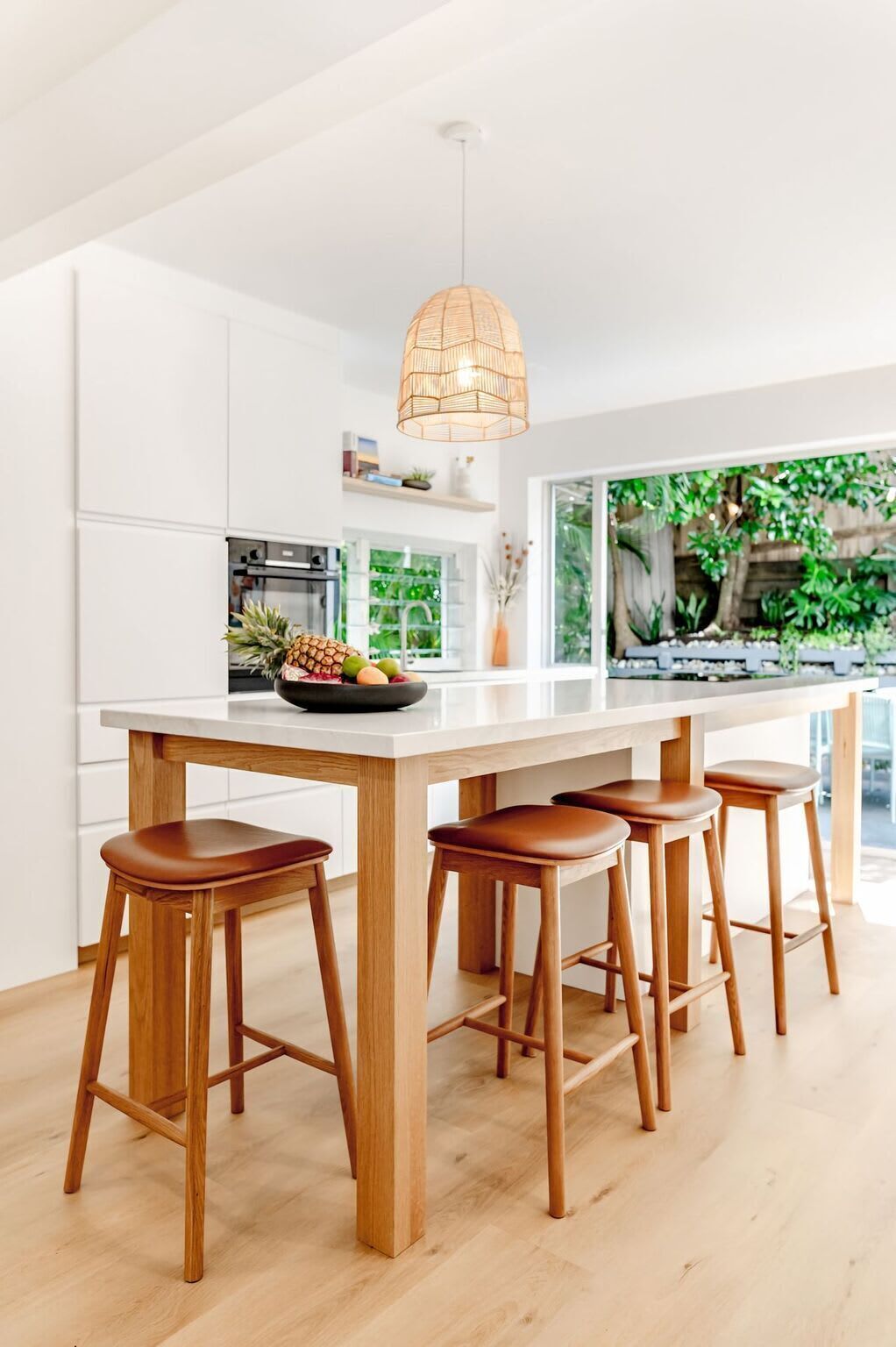 A modern kitchen with a central island, wooden stools, and a hanging light fixture.