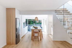 A modern kitchen with a wooden table, bar stools, and a refrigerator. - Serenity on Sunshine Easy Walk to Village Beach (Sunshine Beach)