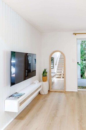 A modern living room with a flat-screen TV mounted on the wall, a white console table with a plant, and a staircase leading to an outdoor area. - Serenity on Sunshine Easy Walk to Village Beach (Sunshine Beach)