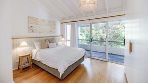 A bedroom with a bed, bedside lamps, a ceiling light, a window with a view, and a door leading to a balcony.