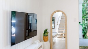 A modern interior with a flat-screen TV mounted on a white wall, a wooden staircase leading to a door, and a potted plant on a small white stool.