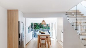 A modern kitchen with a wooden table and stools, a refrigerator, and a glass staircase.