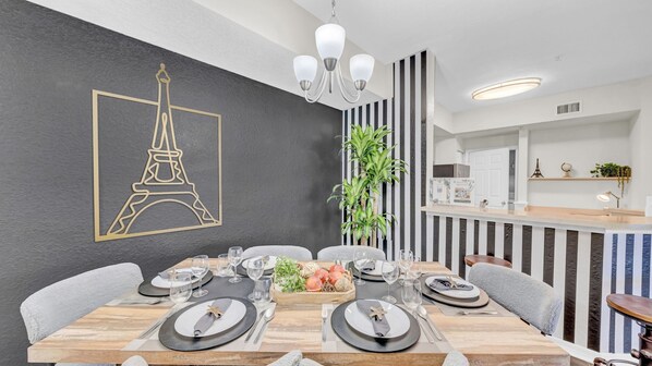 Un comedor con diseño moderno, que presenta una pared a rayas negras y blancas, una araña y vistas hacia la cocina.