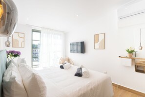A hotel room with a bed, a TV, a window with curtains, and a wall-mounted shelf with a plant. - Loft Centrale by Deserve (Paphos)
