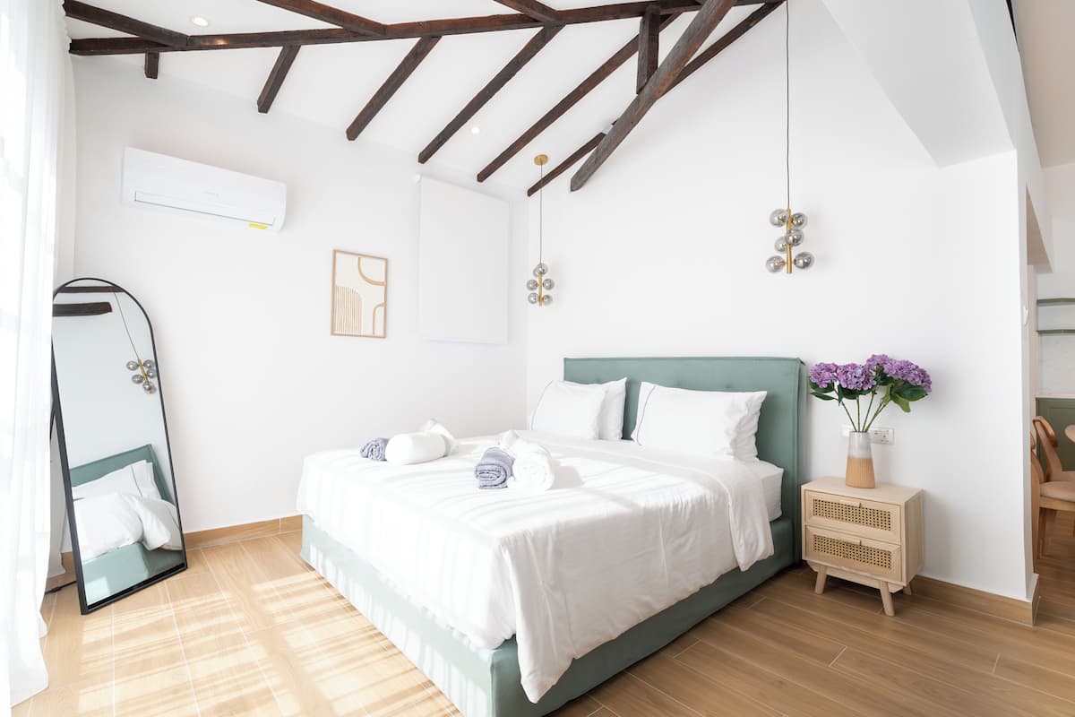A modern bedroom with a bed, a bedside table with a vase of flowers, a mirror, and a ceiling fan.