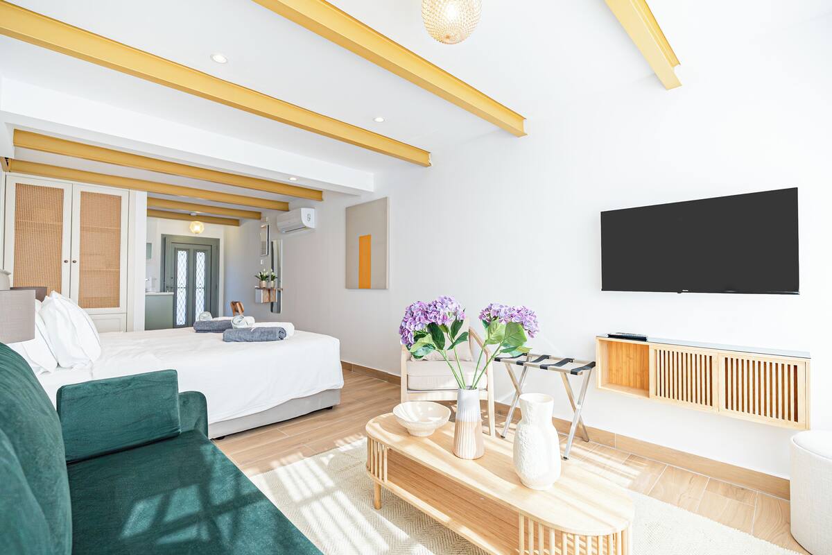 A modern hotel room with a bed, green sofa, wooden coffee table, and a TV mounted on the wall.