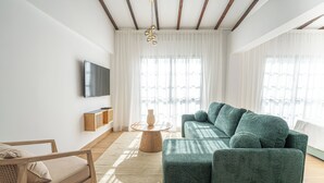 A modern living room with a green sofa, wooden floor, white walls, and a flat-screen TV mounted on the wall. - Loft Centrale by Deserve (Paphos)