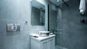 A modern bathroom with a marble backsplash, a round sink, a mirror, and a glass-enclosed shower. - Loft Centrale by Deserve (Paphos)