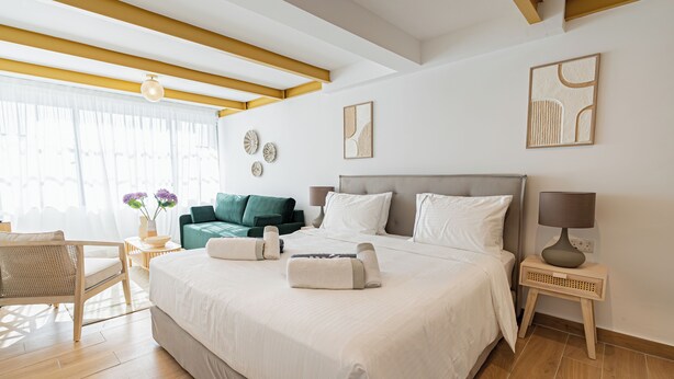 A hotel room with a large bed, a sitting area with a chair and a small table, and artwork on the walls. - Loft Centrale by Deserve (Paphos)