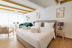 A hotel room with a large bed, a sitting area with a chair and a small table, and artwork on the walls. - Loft Centrale by Deserve (Paphos)