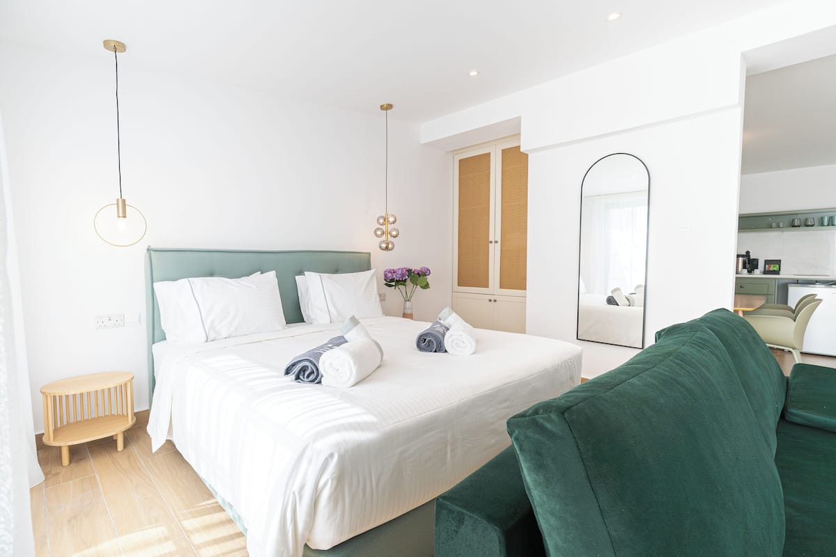 A modern hotel room with a large bed, a green sofa, a small wooden side table, and a bathroom visible through an open door.