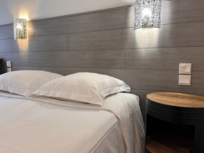 A modern hotel room with a wooden headboard, two bedside lamps, a round wooden side table, and a neatly made bed with white linens. - Hotel Le Lacuzon (Moirans-en-Montagne)