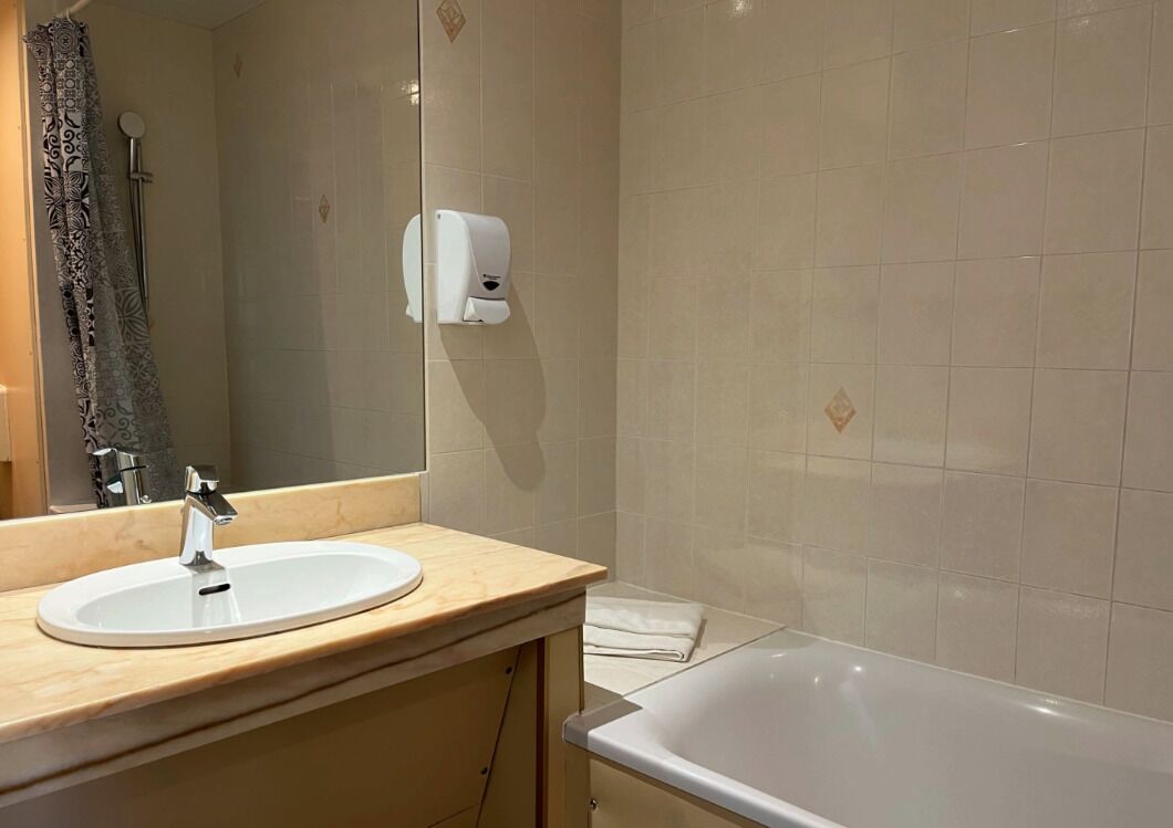 A bathroom with a sink, mirror, hand dryer, and a bathtub.