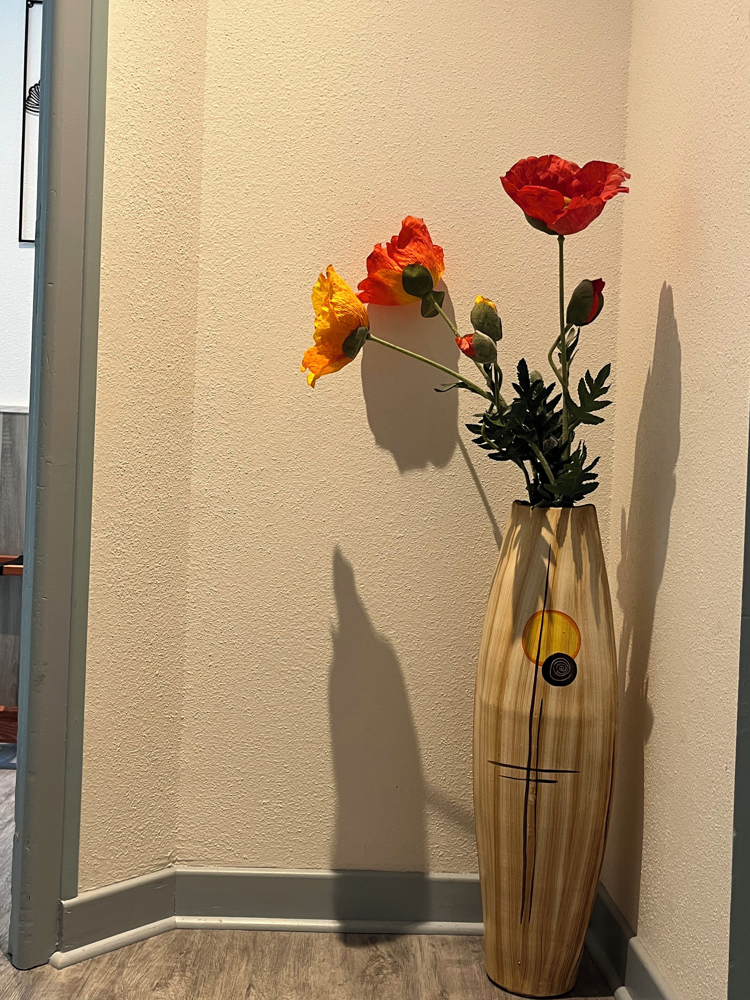 A wooden vase with a geometric design on a textured wall.